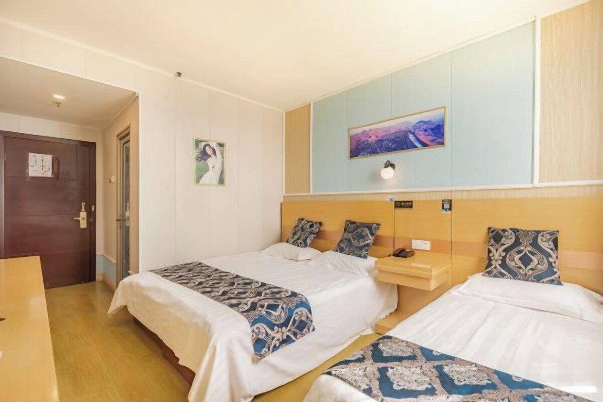 A hotel room with two beds, a nightstand, a wall-mounted light, and a door.