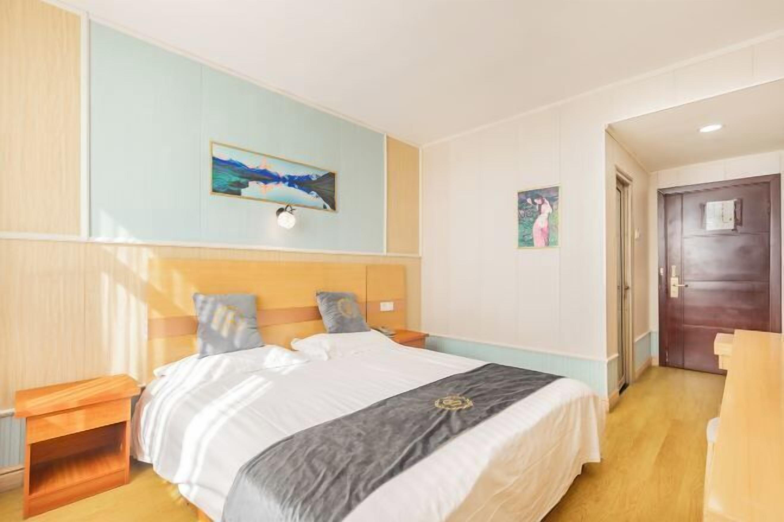 Una habitación de hotel con cama, mesita de noche, un cuadro en la pared y una puerta.