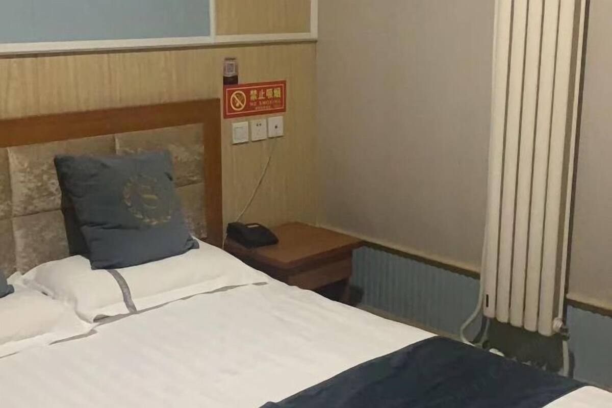 A hotel room with a bed, a nightstand, a phone, and a sign on the wall.