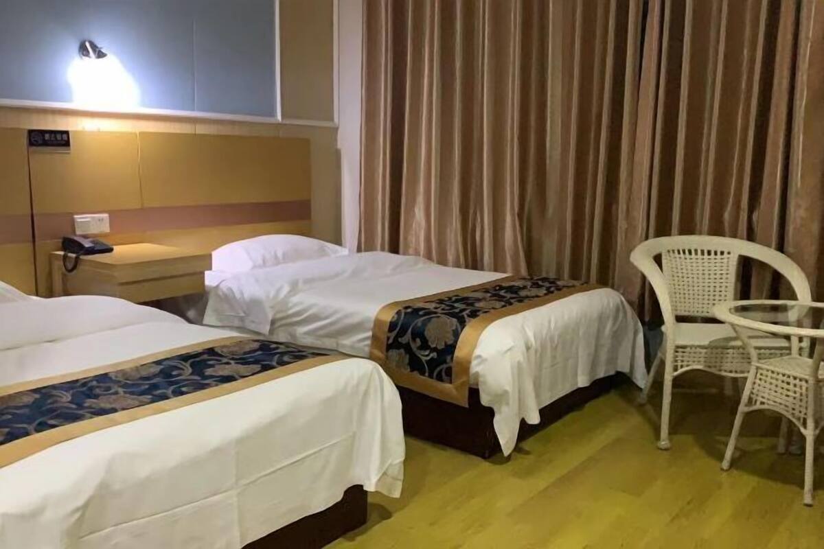 A hotel room with two beds, a small table, a chair, a bedside table with a phone, and a curtain.