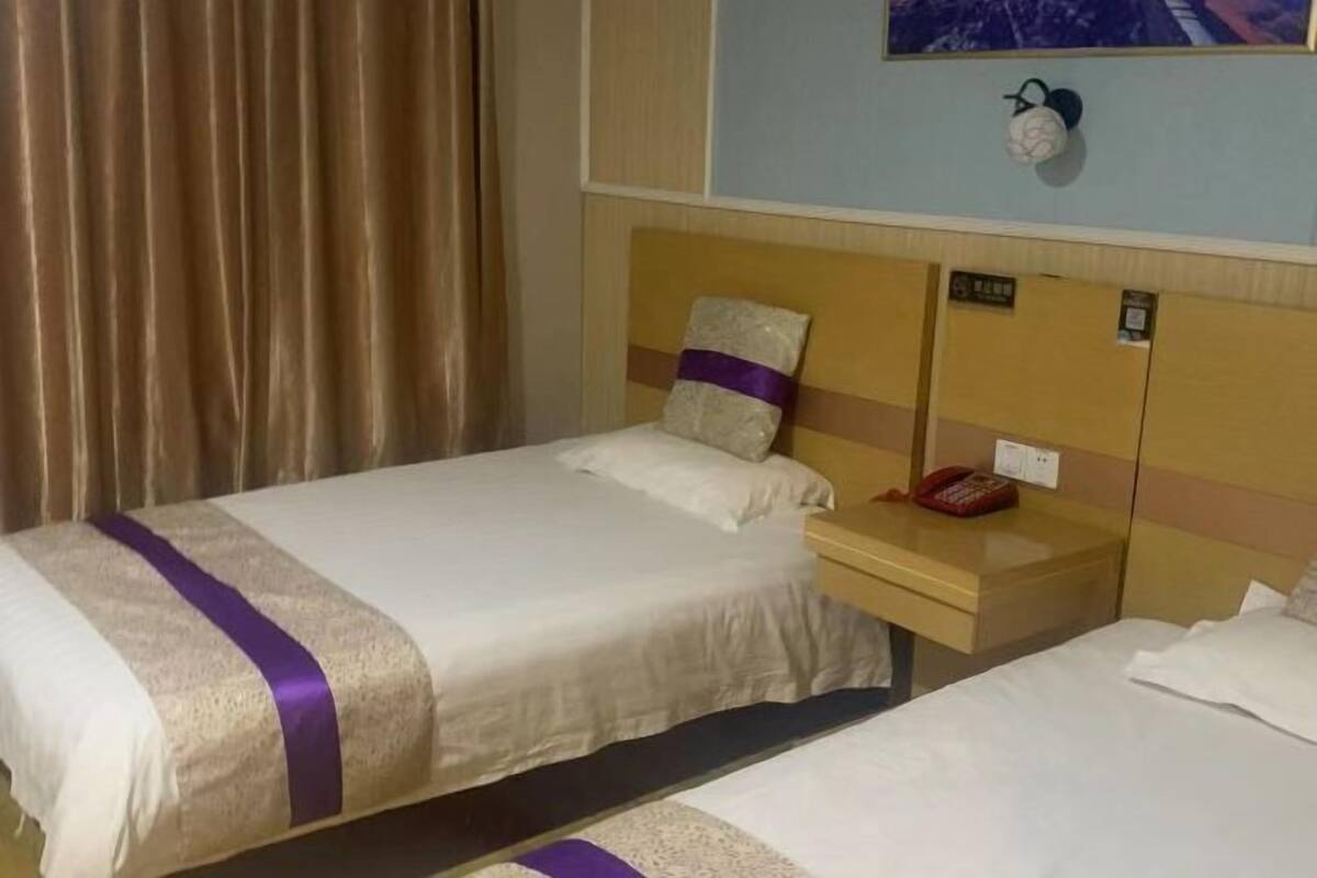 A hotel room with two beds, a wooden nightstand with a telephone, and a wall-mounted light fixture.