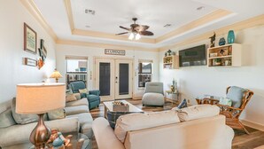 A living room with a ceiling fan, a sofa, a coffee table, and a television on a wall. - Seaside MERRYment - 4 Bedroom + Bonus Room, 2 Bath, Sleeps 16. (Crystal Beach)