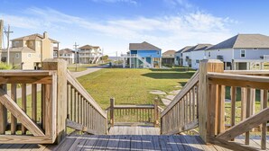A wooden deck leading to a grassy area with houses in the background. - Seaside MERRYment - 4 Bedroom + Bonus Room, 2 Bath, Sleeps 16. (Crystal Beach)