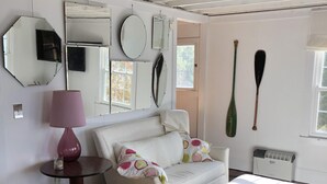 Ein gemütliches Wohnzimmer mit einem weißen Sofa, einem braunen Ledersessel, einem kleinen runden Tisch mit einer rosa Lampe und einem Couchtisch mit einem Tablet.