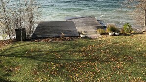 Ein Seeblick mit einem Steg, der ins Wasser ragt, umgeben von Gras und Bäumen.