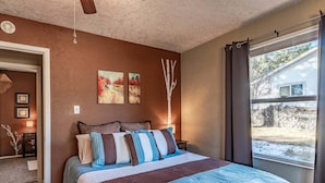 A bedroom with a bed, two paintings, a tree decoration, and a window with a view of a house and yard. - License to Chill | Chill Mode Activated: Hot Tub, Pool Table & Cozy Fireplace (Ruidoso)