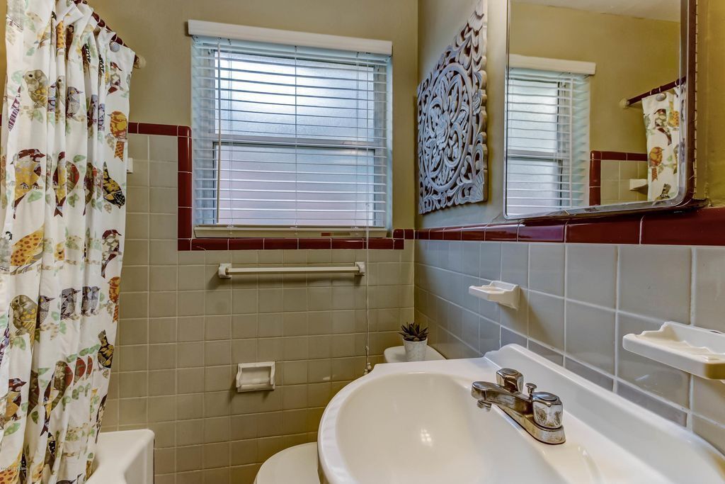 Ein Badezimmer mit einer weißen Badewanne, einer Toilette und einem Fenster mit Jalousien.