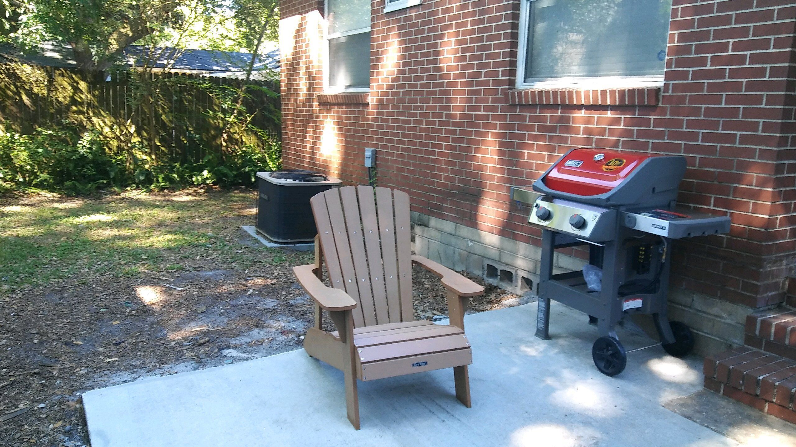 Ein hölzerner Adirondack-Stuhl und ein tragbarer Grill im Hinterhof.