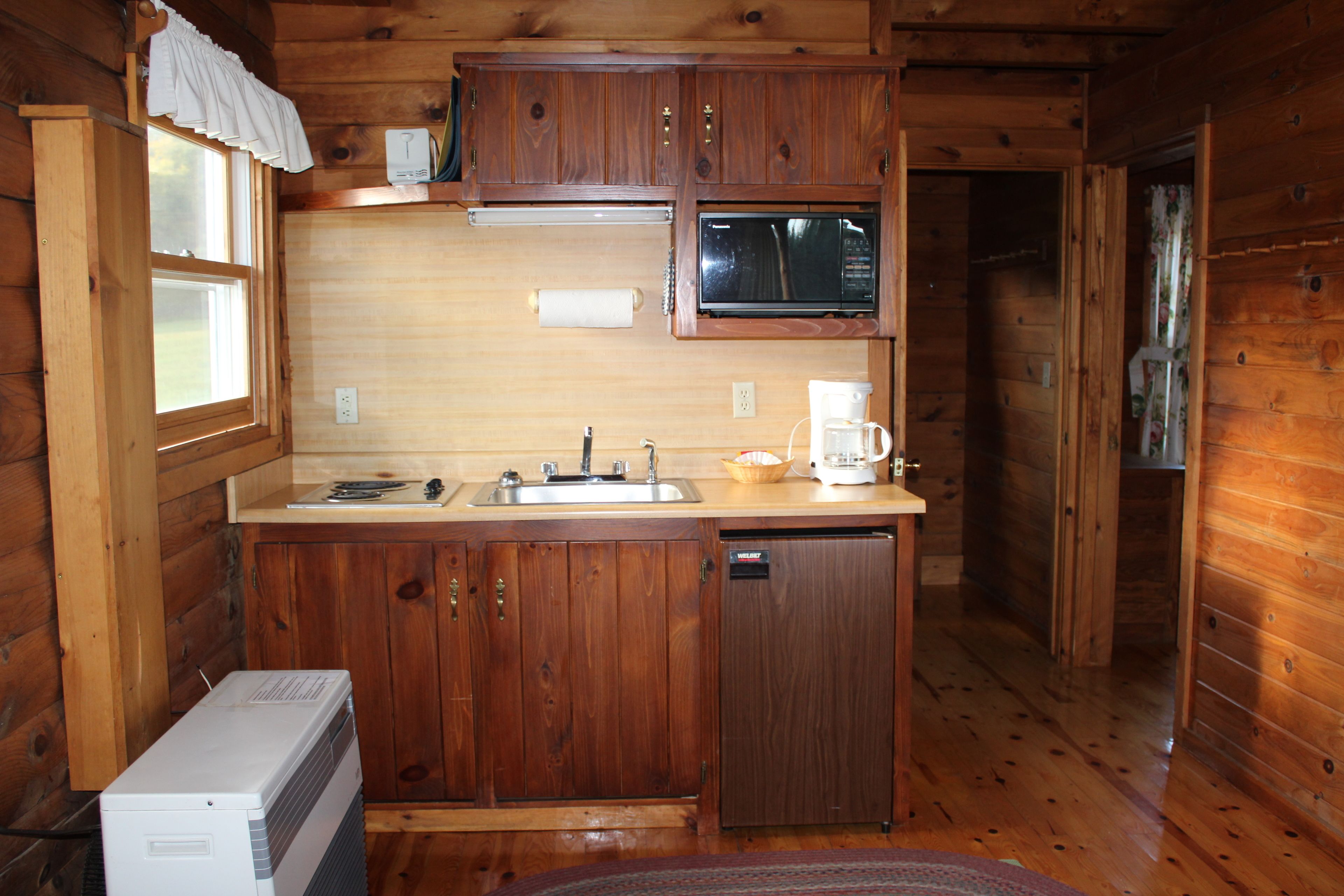 A compact kitchen with wooden cabinets, a microwave, a sink, and a coffee maker.