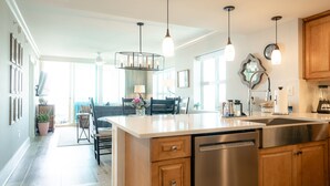 Een moderne keuken met een centraal eiland, roestvrijstalen apparatuur, hanglampen en uitzicht op de eetruimte.