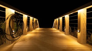Un sendero de madera conduce a un edificio con varias puertas, cada una iluminada por una lámpara.