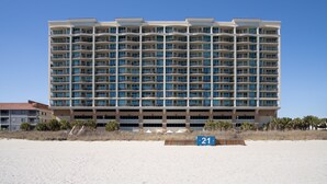 Een hotel met meerdere verdiepingen, balkons, een strand op de voorgrond en een heldere lucht.