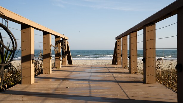 Een houten vlonder die naar het strand leidt, met een helder uitzicht op de zee.