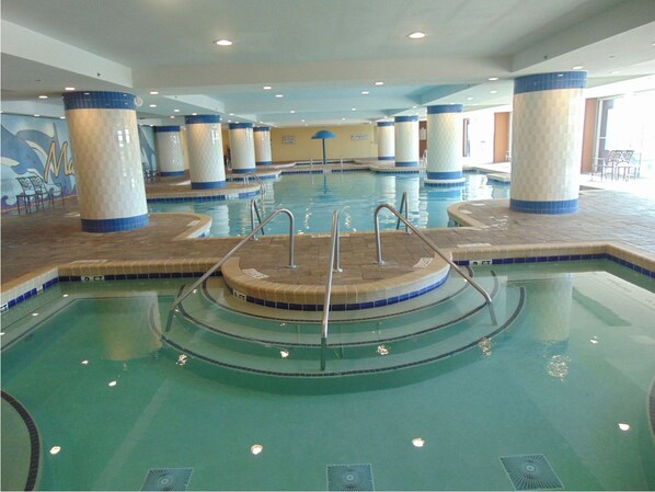 A large indoor swimming pool with multiple lanes, surrounded by tiled pillars and a tiled deck area.