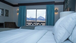 A hotel room with two beds, a view of mountains, and a balcony with a railing.