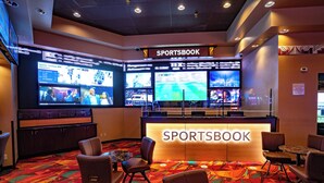 A sports-themed room with multiple screens displaying sports events, a counter labeled 'SPORTSBOK', and comfortable seating.