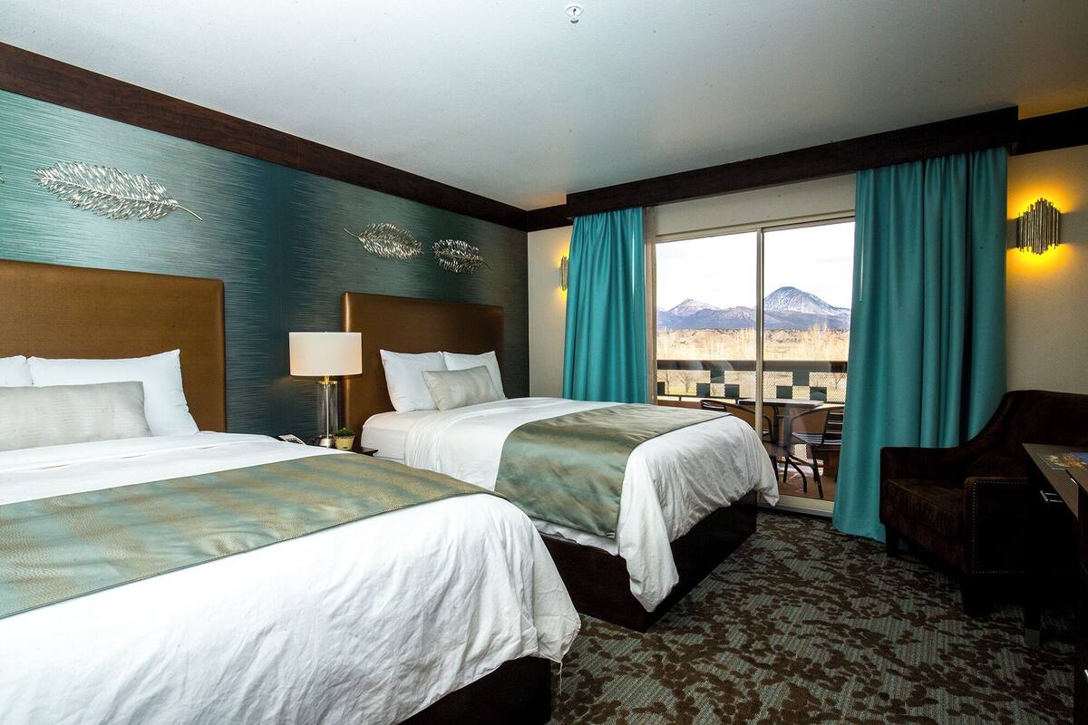Een hotelkamer met twee bedden, een bureau en uitzicht op bergen.