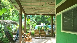 Um alpendre coberto com uma rede, cadeiras de madeira e vista para uma piscina e vegetação.