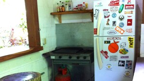 Cozinha compacta com fogão a gás, geladeira decorada com ímãs e um banquinho de madeira.