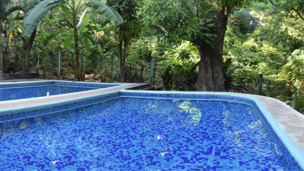Piscina com azulejos de mosaico azul e quatro cadeiras coloridas ao redor.
