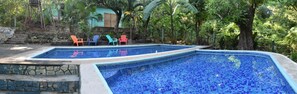 Une piscine aux carreaux de mosaïque bleus, entourée de quatre chaises colorées.