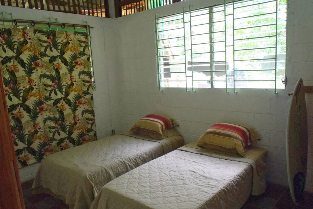 Une chambre avec deux lits simples, une fenêtre avec des barreaux et un rideau à motifs floraux.