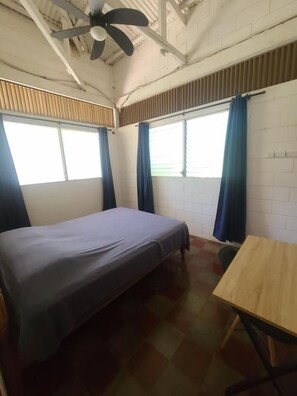 A room with a bed, a table, and a ceiling fan.