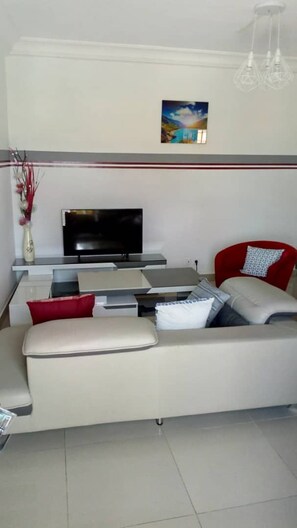 A modern living room with a flat-screen TV, a sofa, and a red chair. - Les Résidences Malaïka (Libreville)