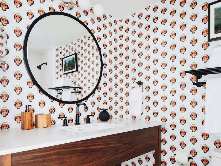 A bathroom with a white sink, wooden vanity, and a mirror. The wall features a repeating pattern of monkey faces.