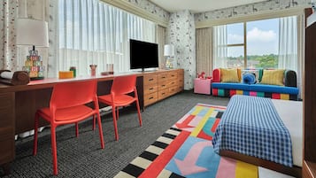 Quarto com escrivaninha, televisão, sofá colorido e cama.