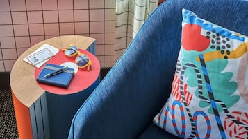 Un fauteuil bleu avec un coussin coloré, une petite table ronde sur laquelle se trouvent un passeport, des lunettes de soleil et un carnet.