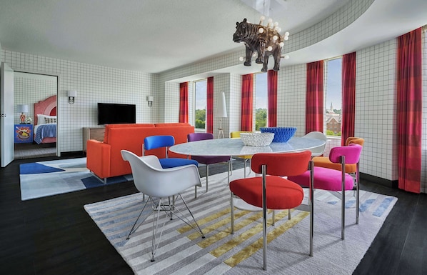 A modern hotel room with a dining area, a TV, and a large window with curtains.