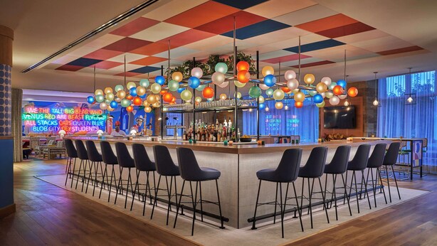 Una zona de bar con techo a cuadros, luces colgantes de colores y un letrero de neón al fondo.