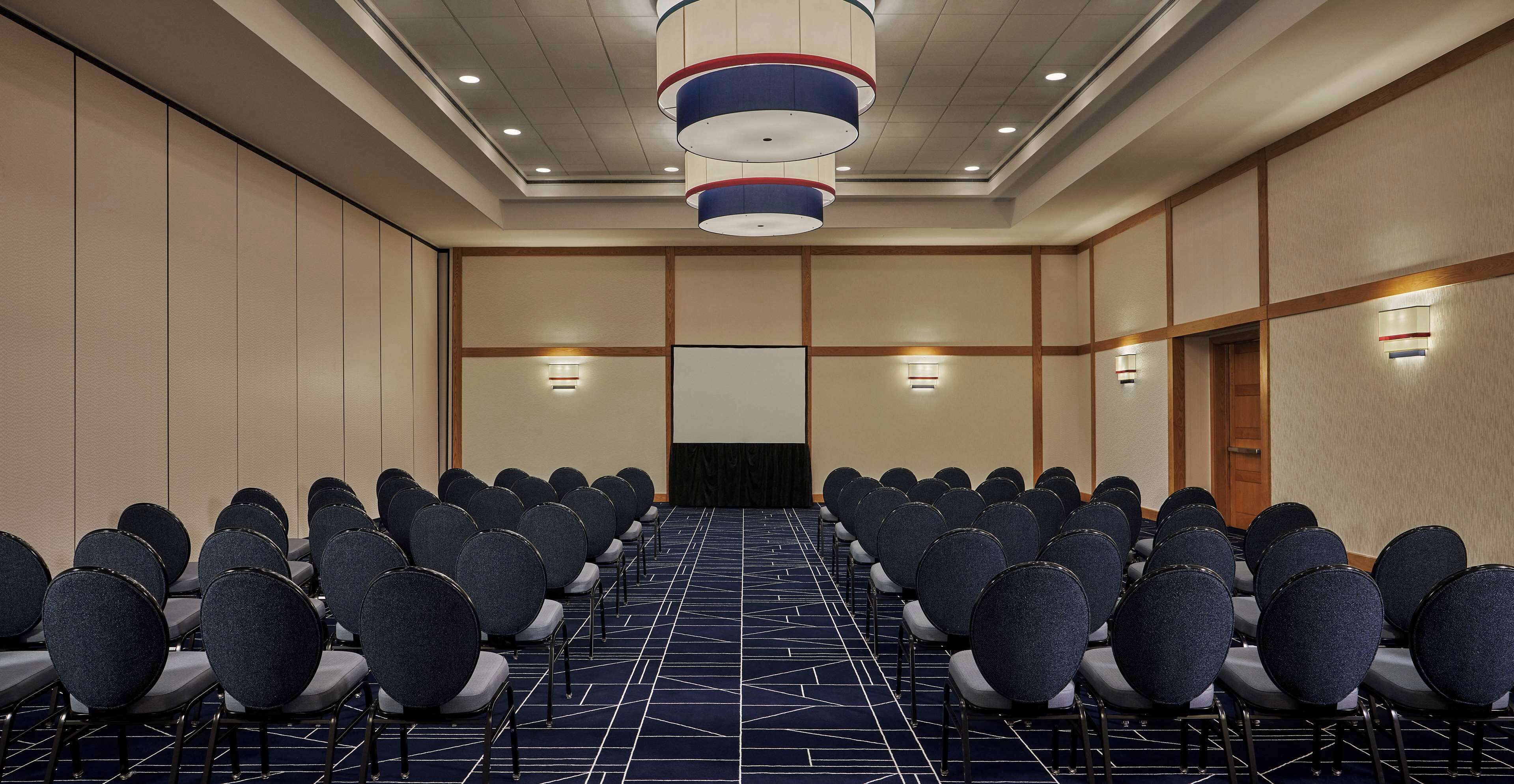 Une salle de conférence avec des rangées de chaises, une moquette à motifs et un plafond doté d’un éclairage encastré.