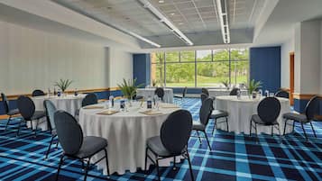 Un salón de conferencias con mesas redondas, sillas y vistas a un paisaje verde a través de amplios ventanales.