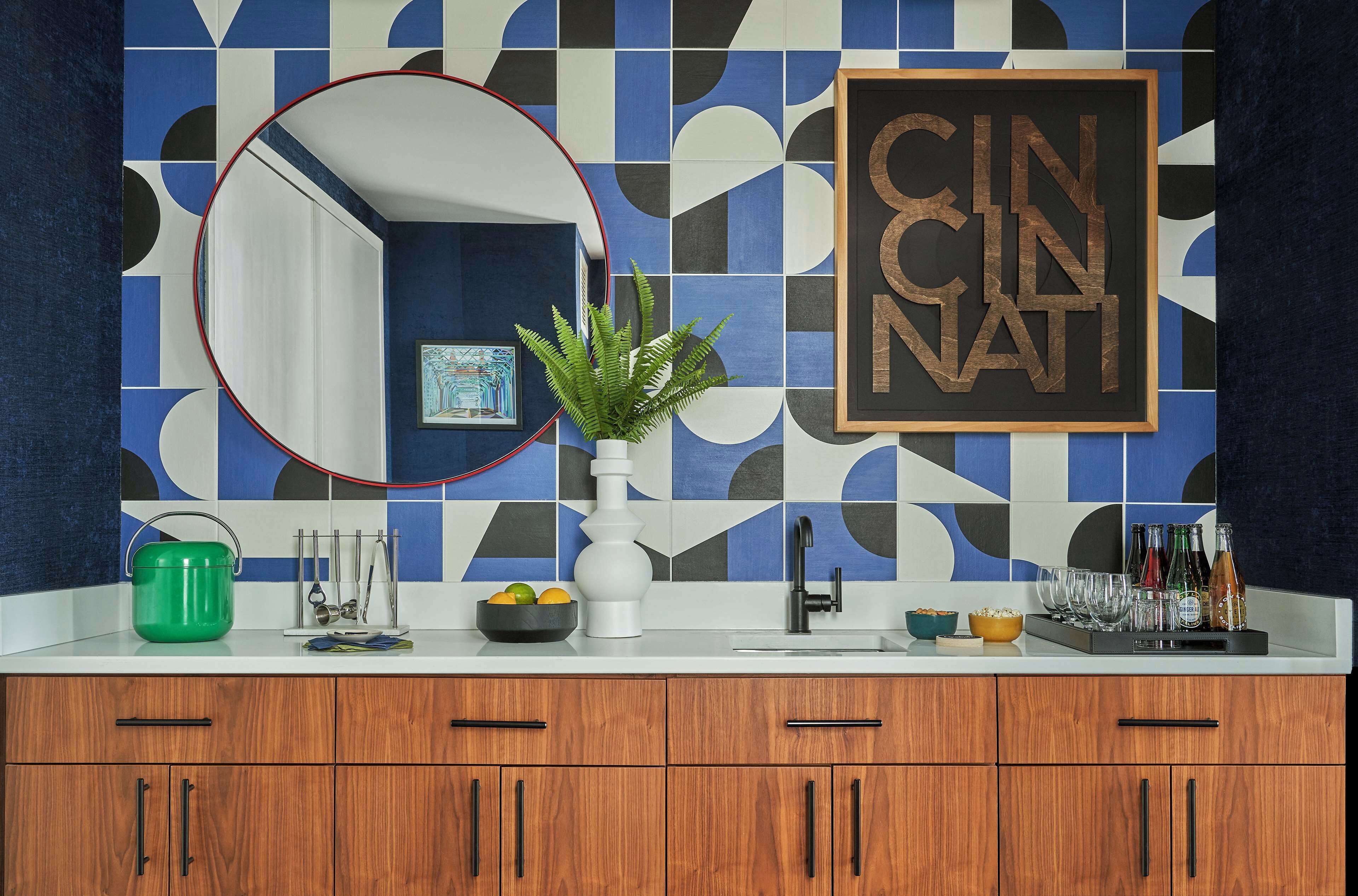 A kitchen with a geometric tile backsplash, a framed sign, a green pot, and various kitchen utensils.