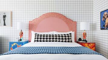 Una cama bien hecha con una colcha a cuadros, un cabecero tapizado en rosa y dos mesitas de noche con lámparas y figuritas de astronautas.