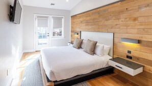 Een moderne slaapkamer met een groot bed, een wand van houten panelen, nachtkastjes en een aan de muur bevestigde televisie.