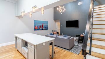 Un salon moderne avec un coin repas blanc, un canapé gris et un escalier.