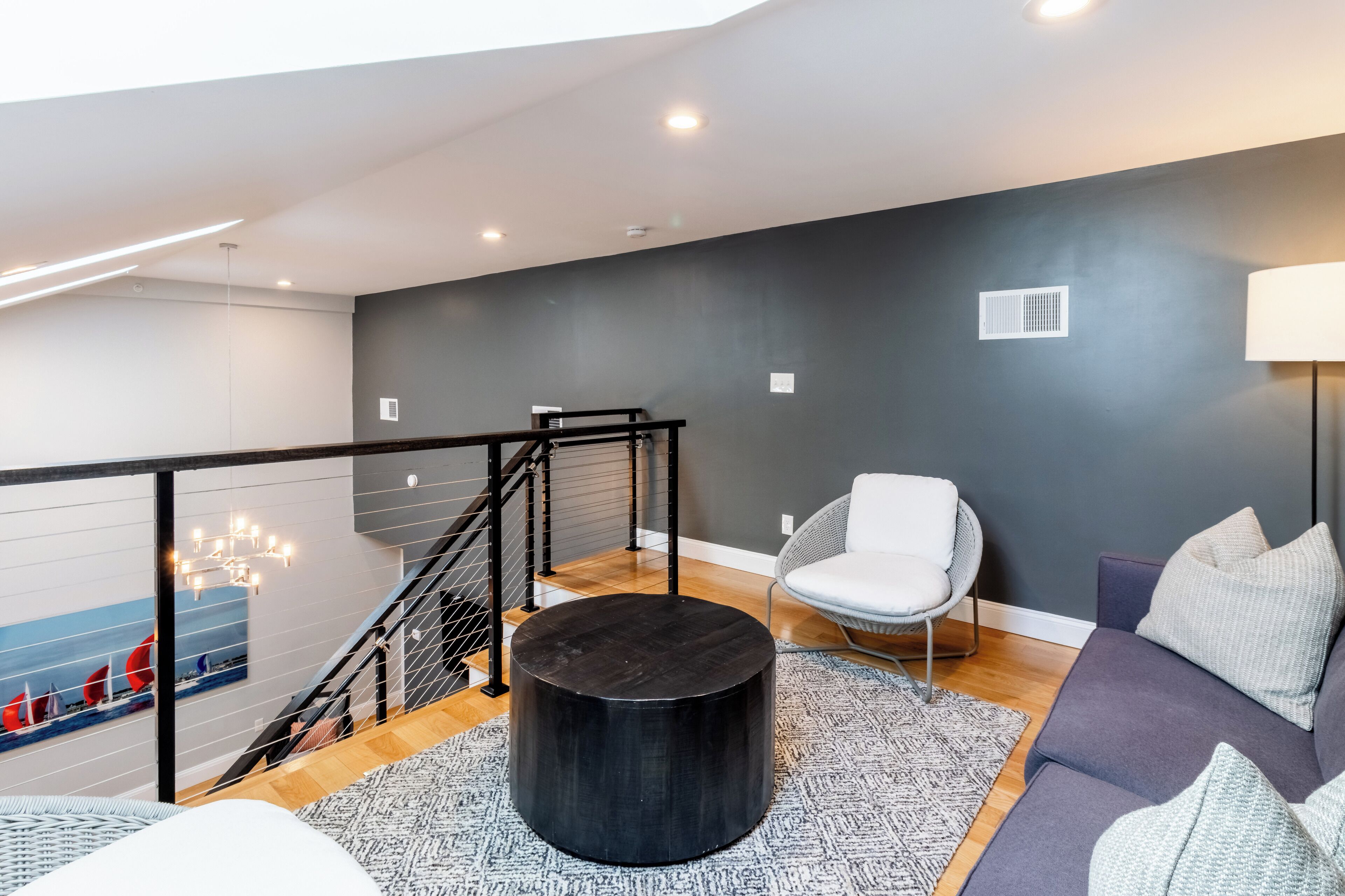 A modern living room with a grey wall, a round black coffee table, a grey sofa, and a white chair.