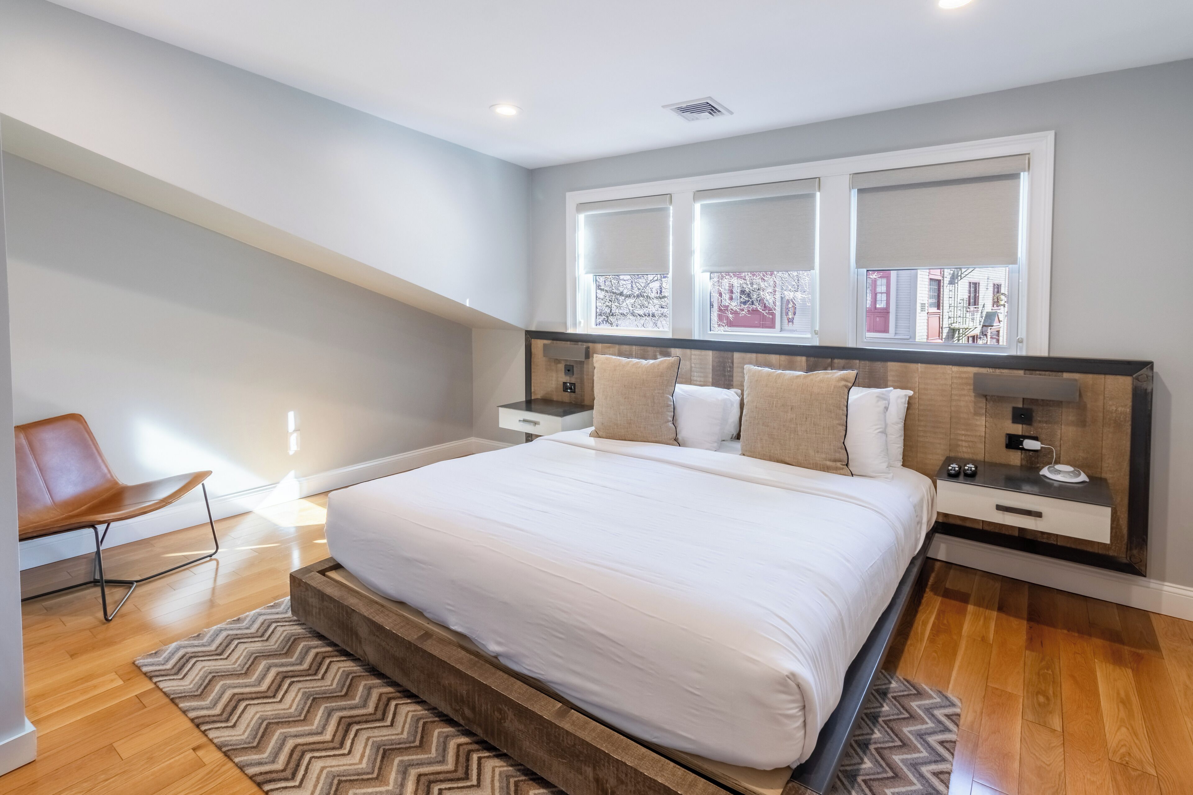 Un dormitorio moderno con una cama grande, cabecera de madera, mesitas de noche y vistas a la ciudad a través de amplios ventanales.
