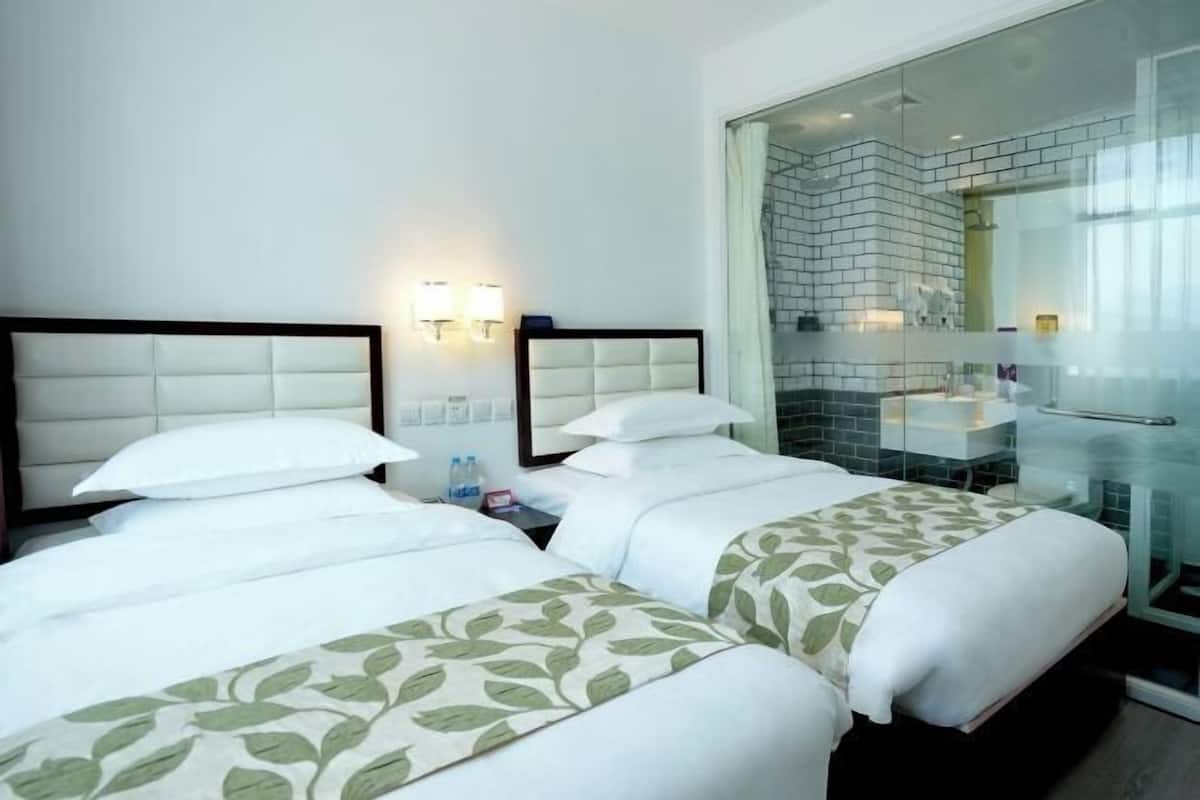 A hotel room with two beds, a glass shower enclosure, and a white-tiled bathroom.