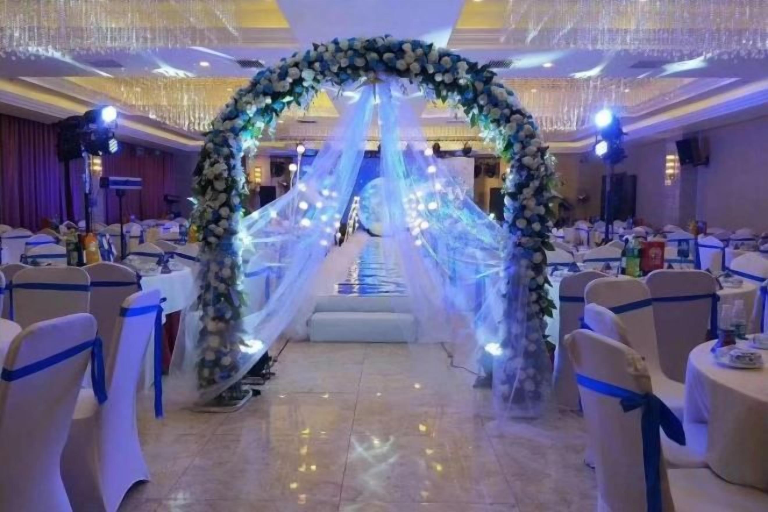 A banquet hall with round tables and chairs, a floral archway, and a chandelier.