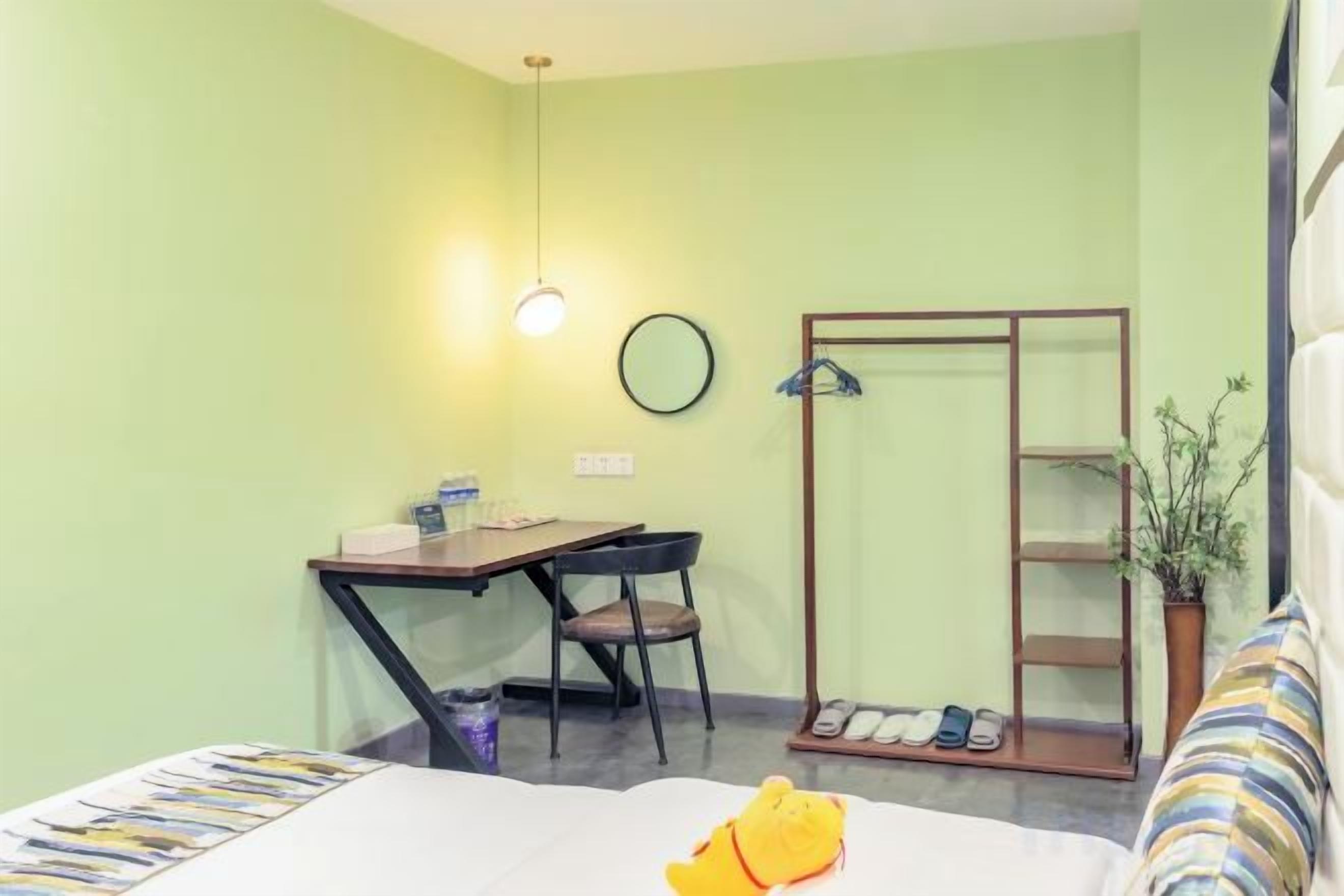 A room with a bed, a desk, a chair, a mirror, and a shoe rack.
