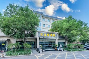Un hotel rodeado de árboles y con un área de estacionamiento, con un letrero en idioma extranjero.