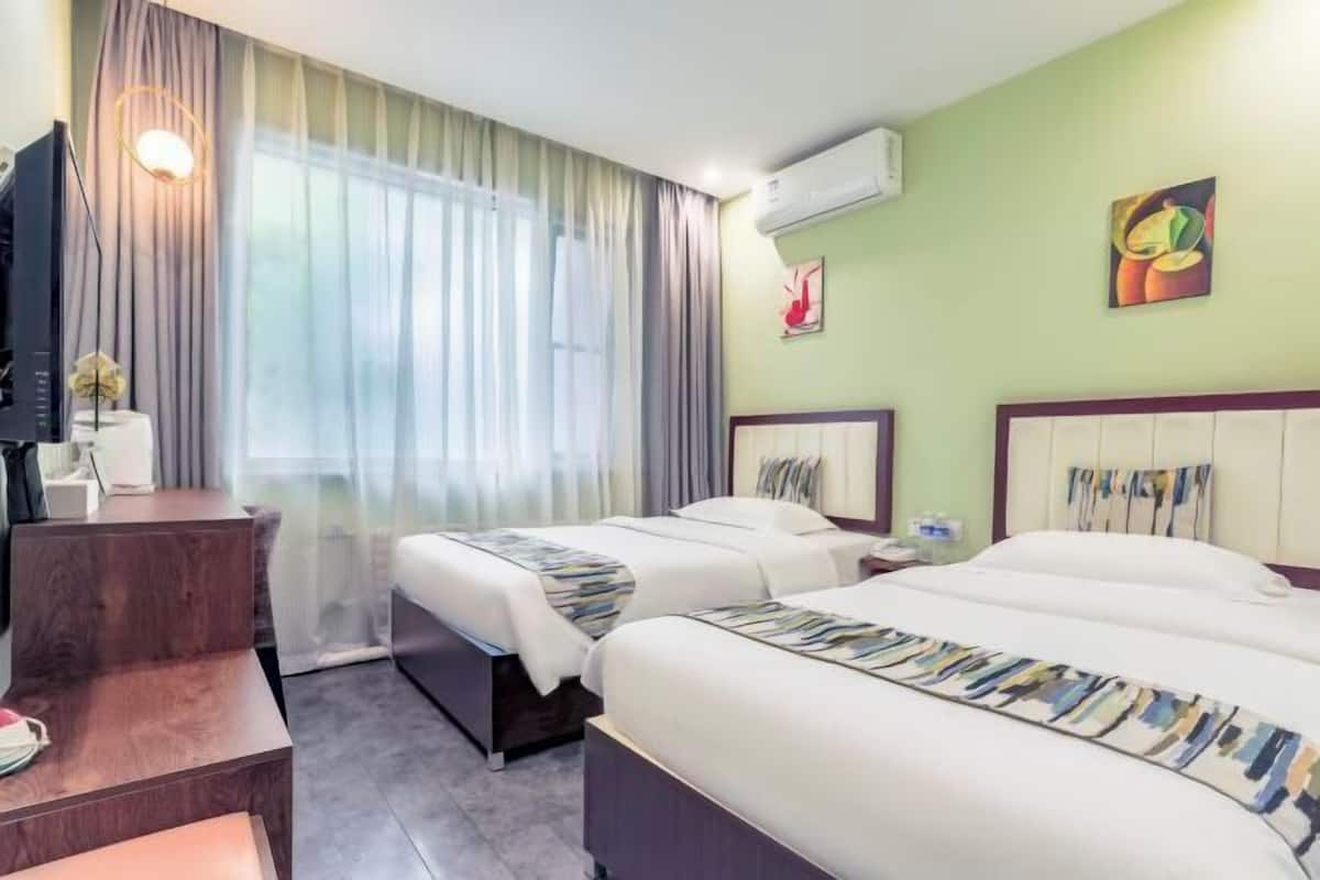 A hotel room with two beds, a desk, a TV, and a window with curtains.