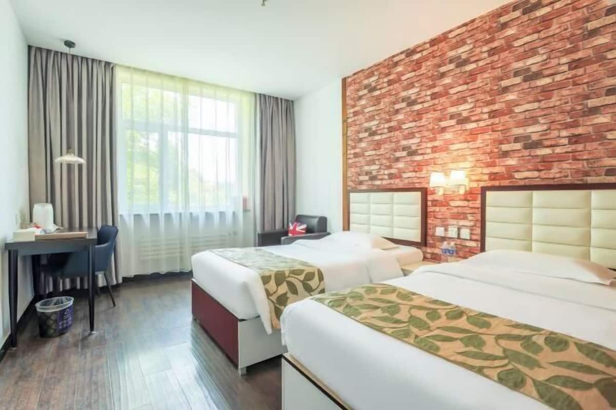 A hotel room with two beds, a desk, a chair, and a brick-patterned wall.