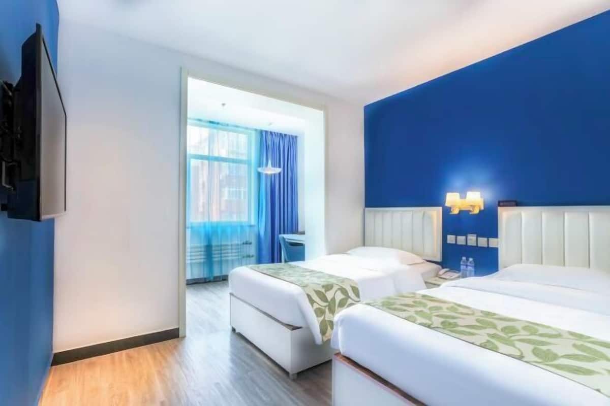 A hotel room with two beds, a blue accent wall, and a view of the outside through a large window.