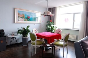 Un comedor con una mesa roja, sillas blancas, un ventilador de techo y un amplio ventanal con cortinas.