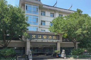 A hotel with a traditional architectural style, featuring a prominent entrance with a sign, a statue in front, and a well-maintained garden area. - Northstar Business Linkage Hotel (Beijing)